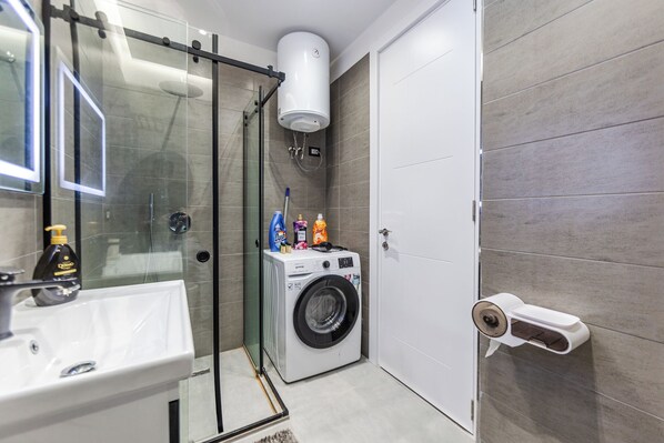 Un baño moderno con cabina de ducha de vidrio, lavadora y un dispensador de papel higiénico en la pared.
