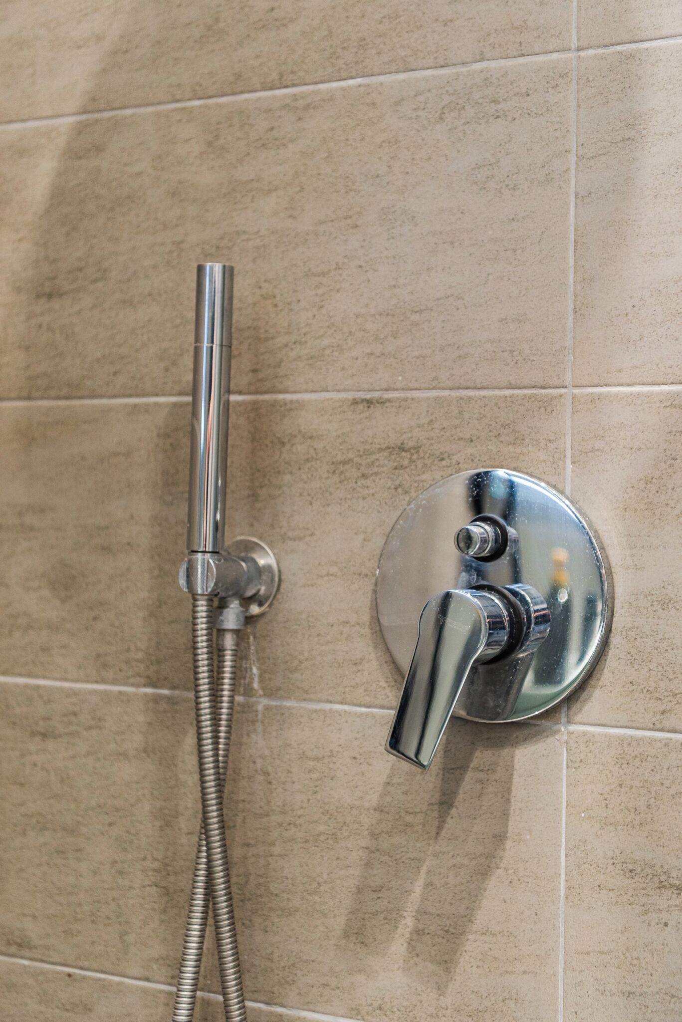 Une douche avec un robinet et un tuyau en chrome, fixés sur un mur carrelé.