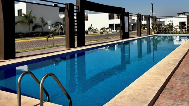 Une piscine à l’eau d’un bleu cristallin, entourée d’une terrasse carrelée et bordée de structures architecturales modernes.