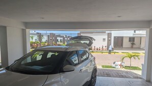 Une voiture blanche est garée à l’intérieur d’un espace abrité, d’où l’on aperçoit un bâtiment et un espace paysager à l’extérieur.