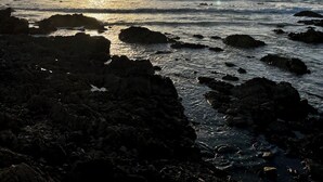 Un coucher de soleil sur la côte, avec un paysage rocheux et une mer calme.