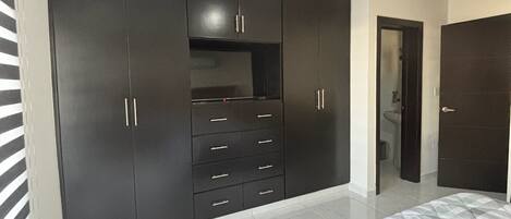 A bedroom with a large wardrobe, a bed, and a bathroom visible through an open door.