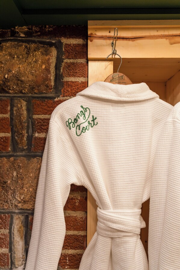 Une robe blanche ornée d’une broderie représentant « Bang’s Court » dans le dos, suspendue contre un mur de briques.