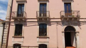 Un bâtiment rose avec trois fenêtres, une porte et un petit balcon orné de plantes.