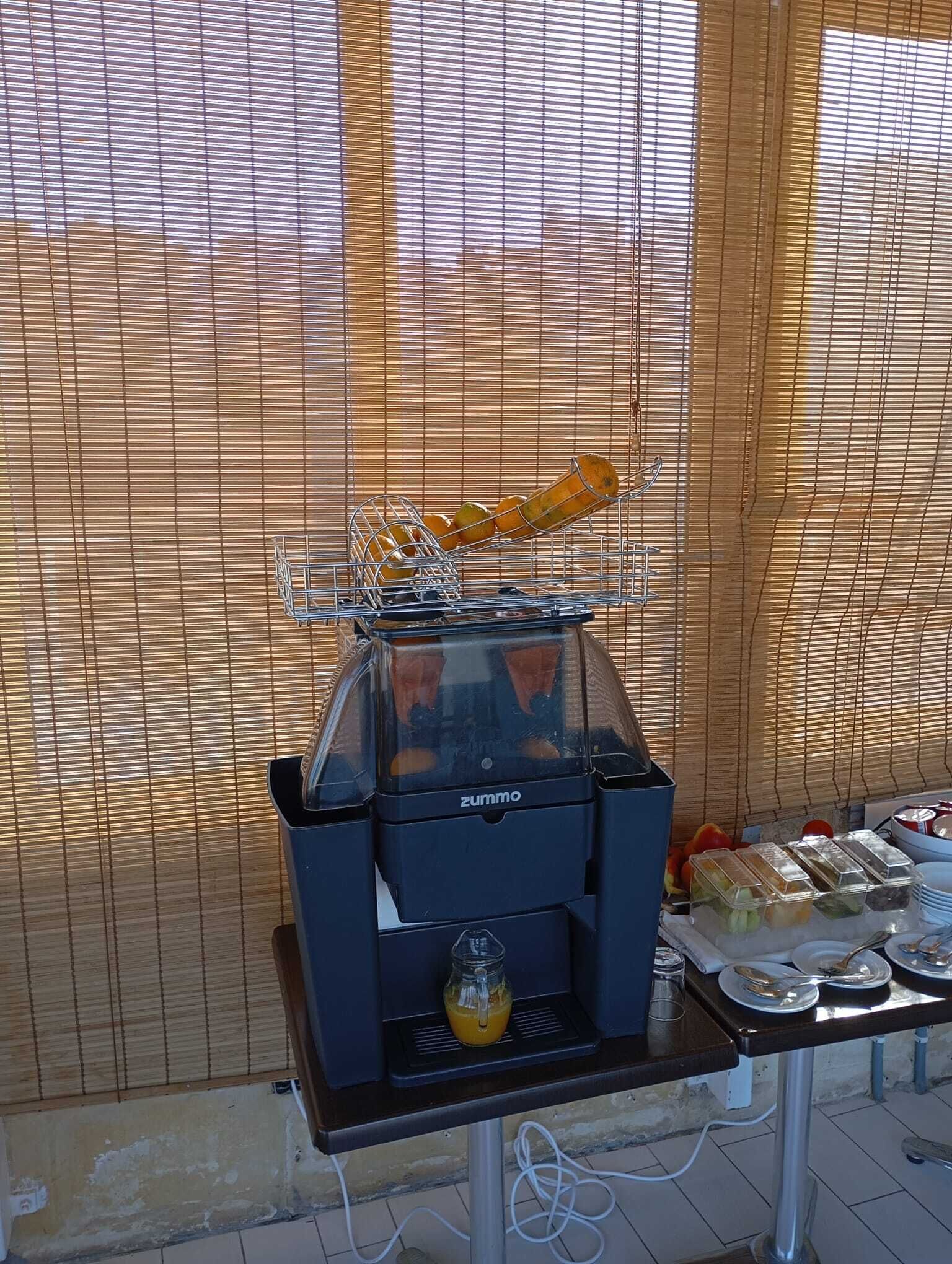 A food service station with a grill, a juicer, and a tray of food items.