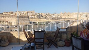 A terrace with a table and chairs, overlooking a harbor with boats and buildings. - Villa Del Porto  (Kalkara)