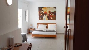 A hotel room with a bed, a dining table with chairs, a painting on the wall, and a ceiling light. - Villa Del Porto  (Kalkara)