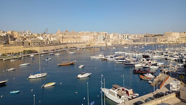 A marina with numerous boats docked, a clear sky, and a cityscape with historical buildings in the background. - Villa Del Porto  (Kalkara)