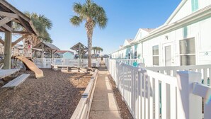Une propriété située en bord de mer, dotée d’une terrasse en bois, d’un palmier et d’une clôture blanche.