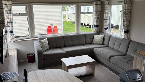 Ein modernes Wohnmobil-Interieur mit einer Eckcouch, einem Holztisch und einem Mülleimer.