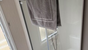 Ein Badezimmer mit Duschkabine aus Glas, einer weißen Toilette und einem Handtuchhalter mit blauem Handtuch.