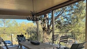 Un patio al aire libre con una mesa de madera y sillas de metal, rodeado por una cerca metálica y árboles.