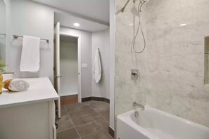 Ein modernes Badezimmer mit einer Badewanne, einer Dusche und einem WC. Ein Handtuchhalter mit Handtüchern und ein kleiner Tisch mit einem Handtuch und einer Pflanze.