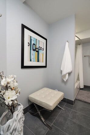 Ein modernes Badezimmer mit einer weißen Toilette, einem gerahmten abstrakten Gemälde, einem weißen Handtuch an der Wand und einer weißen Sitzbank.