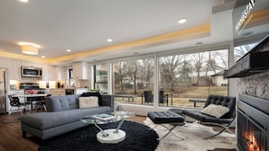 A modern living room with a fireplace, a dining area, and a kitchen. - Bassett Creek Retreat (Golden Valley)