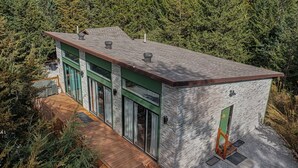 Una casa moderna con fachada de piedra, ventanas amplias y una terraza de madera.