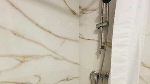 A bathroom with a marble wall, a shower with a handheld showerhead, and a white shower curtain. - Port du Levant (Toulon)