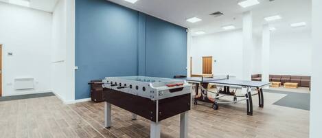 A spacious room with a foosball table, ping pong table, and a blue accent wall.
