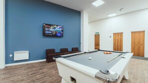 A pool table in a room with a blue wall, a mounted TV, and a seating area with brown chairs. - Student Only Lomax Halls (Stoke-on-Trent)