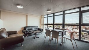 A modern room with a leather sofa, a small table, and chairs, large windows with a city view. - Student Only Lomax Halls (Stoke-on-Trent)