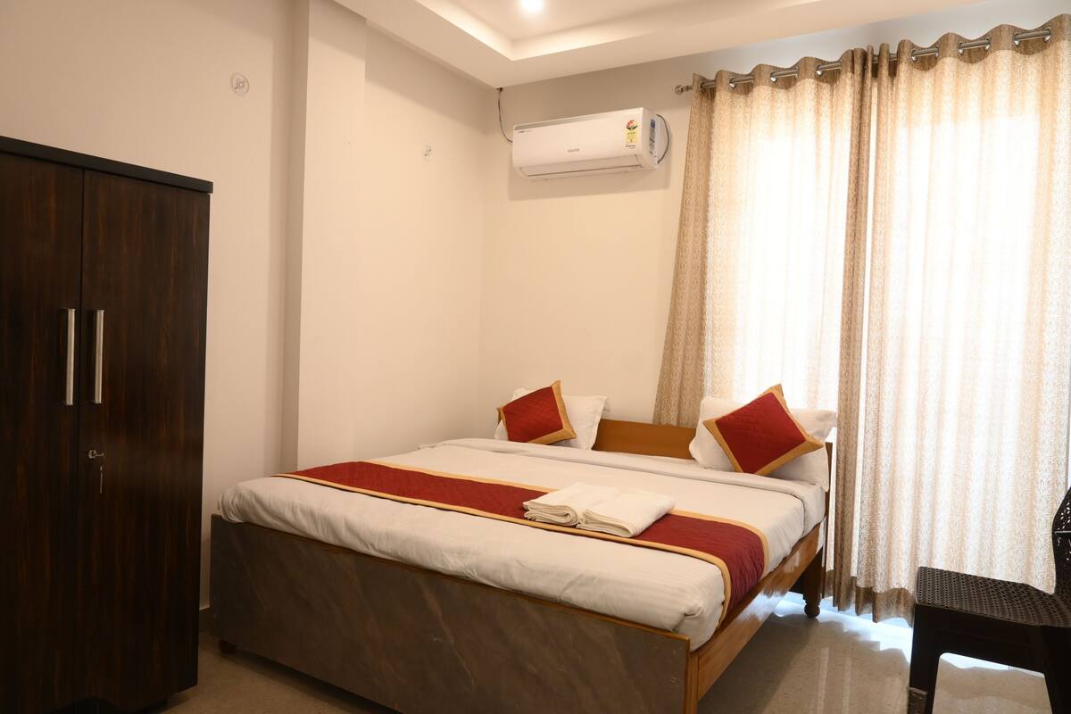 A hotel room with a bed, a wardrobe, an air conditioning unit, and a window with curtains.