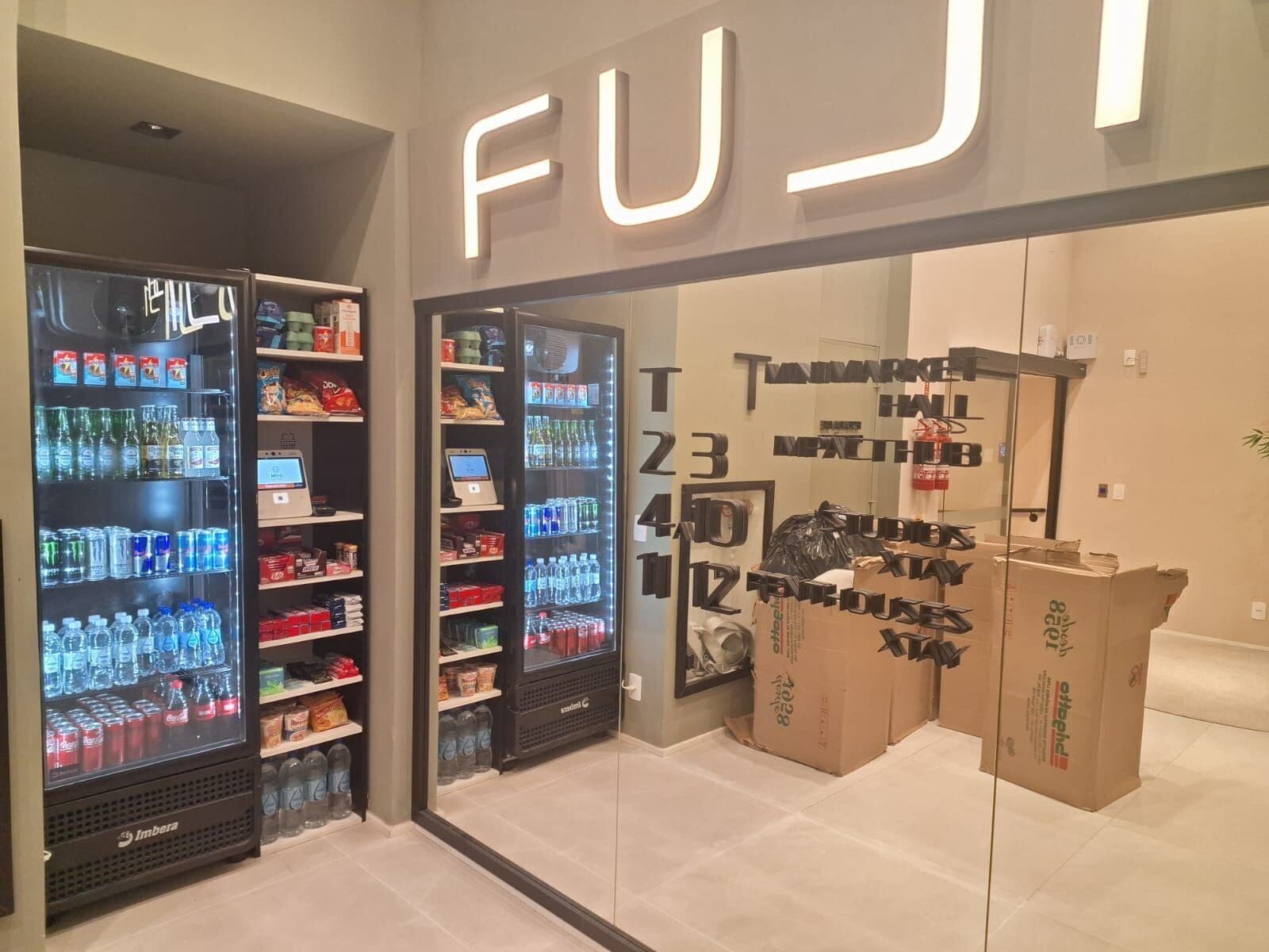 A FUJI store with vending machines, shelves stocked with snacks and beverages, and cardboard boxes stacked outside.