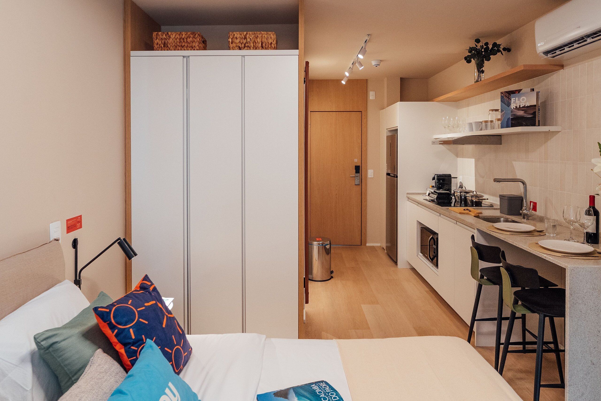 A compact hotel room with a bed, a small kitchenette, and a separate bathroom.