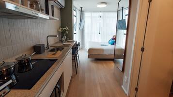 Cocina pequeña con estufa, lavamanos y taburetes de bar. Se ve una cama con almohada azul a través de una puerta abierta.