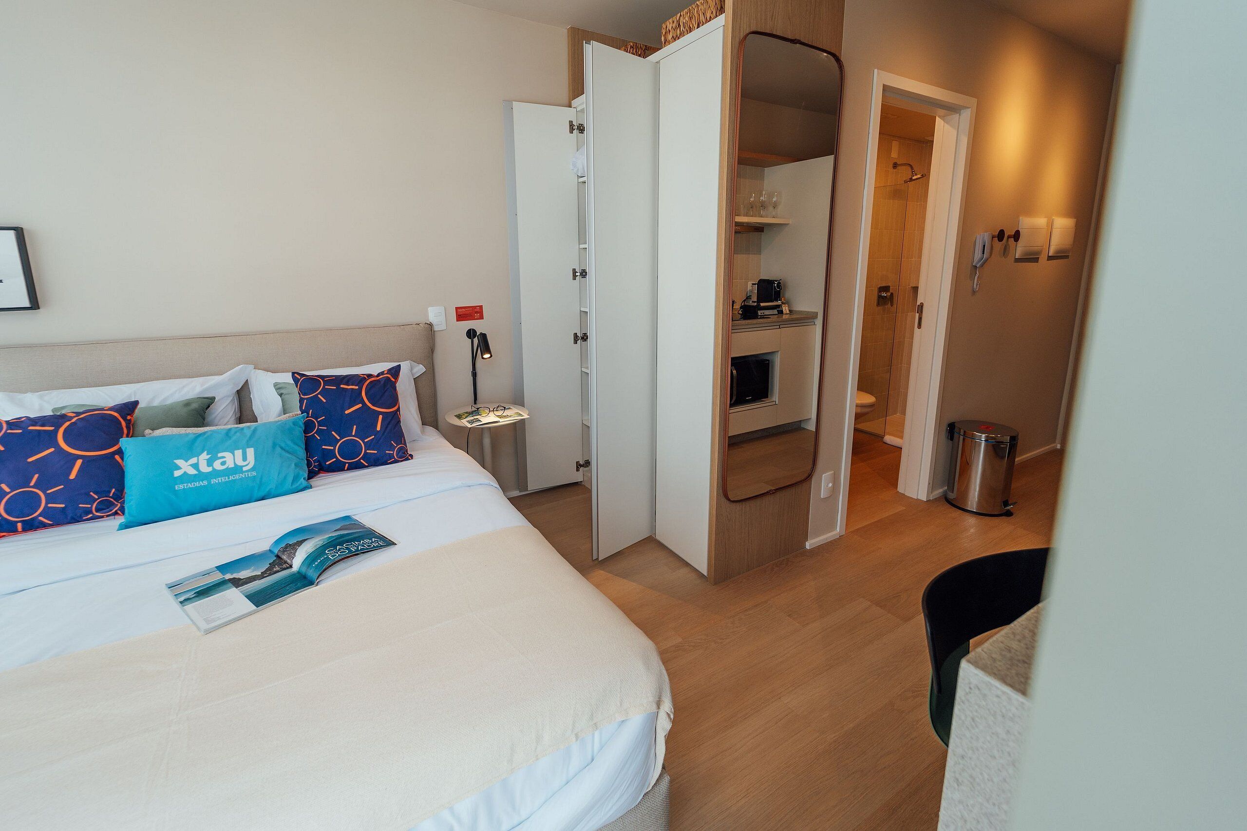 Een hotelkamer met een bed, nachtkastje, leeslamp, een badkamer zichtbaar door een open deur en een prullenbak.