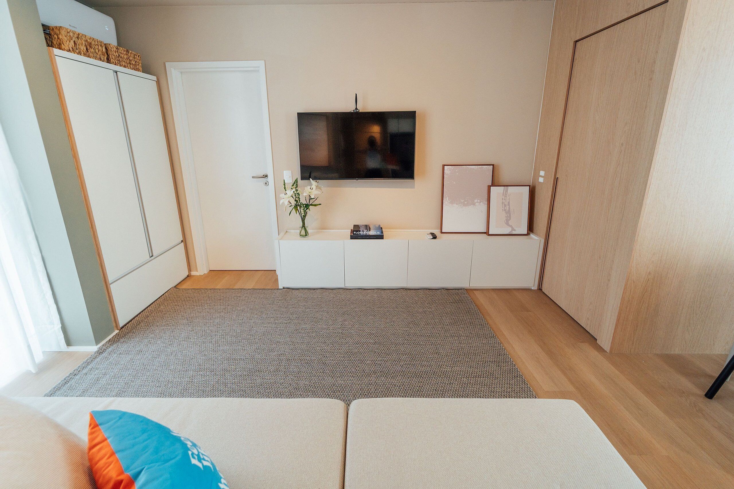 A modern room with a flat-screen TV mounted on the wall, a sofa, a small table with a vase, and a cabinet.