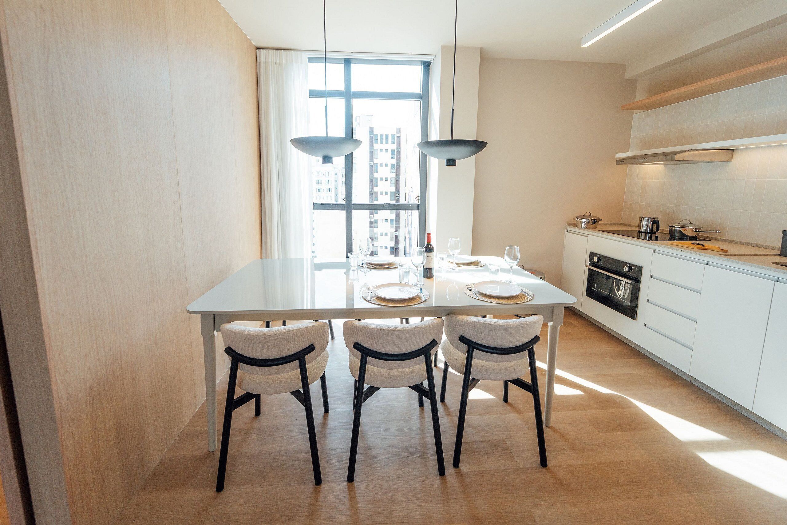 A modern kitchen with white cabinets, a large window, and a dining area with a table set for four.