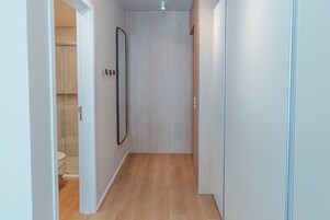Um corredor estreito com soalho de madeira, uma porta para um banheiro e um espelho na parede.