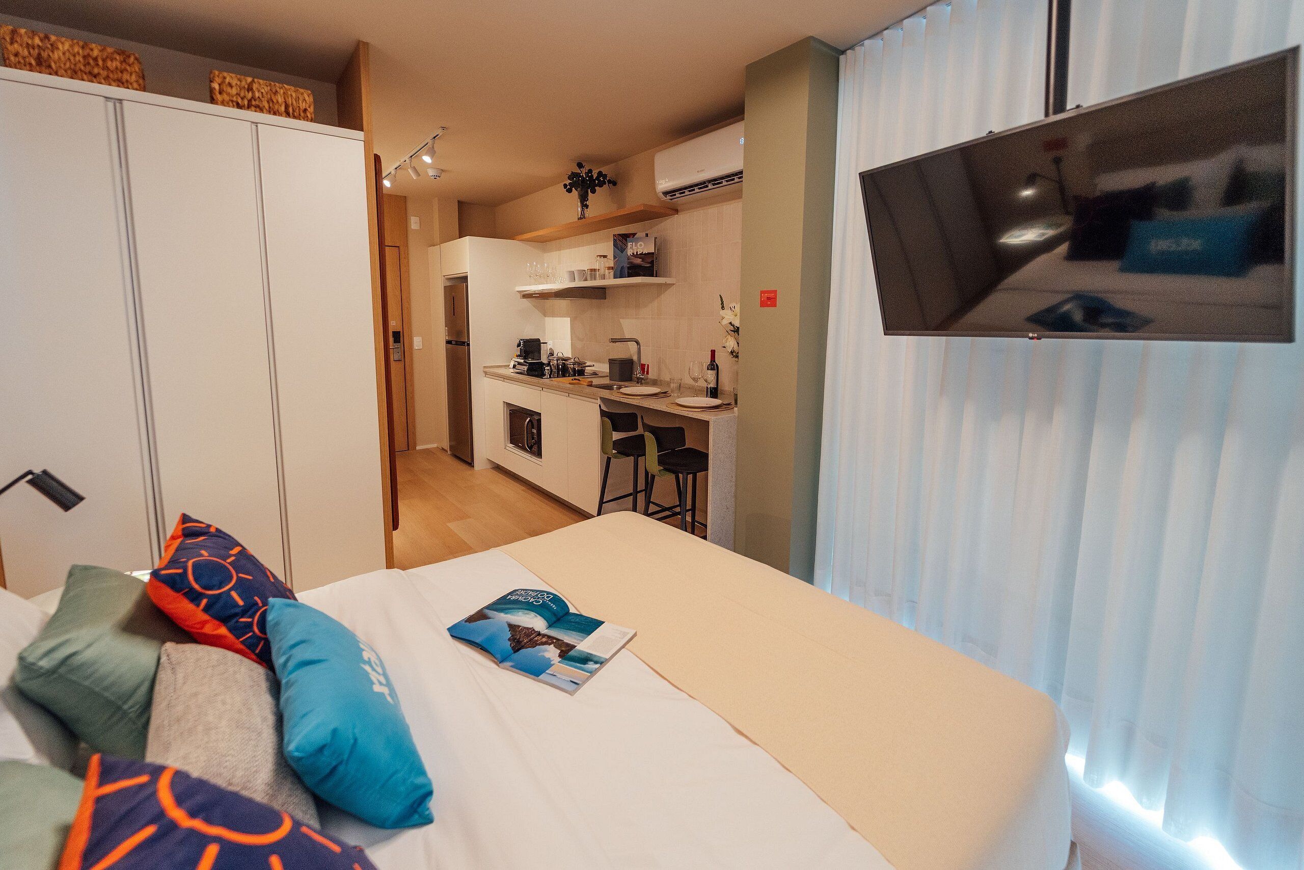 Une chambre d’hôtel équipée d’un lit, d’oreillers, d’un livre, d’une télévision, d’une kitchenette et d’une salle de bain.