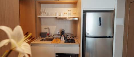A compact kitchen with a stainless steel refrigerator, a microwave, a gas stove, and a wooden cutting board.