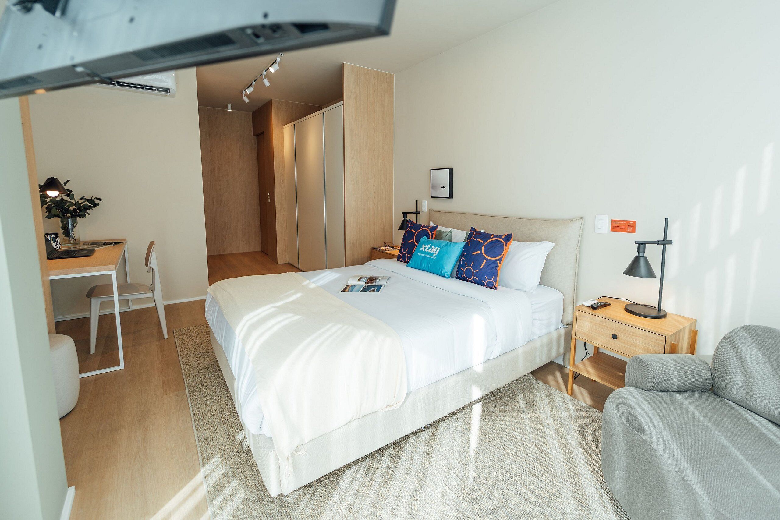 Une chambre d’hôtel moderne, dotée d’un grand lit, d’un bureau, d’une chaise et d’une table de chevet avec une lampe.