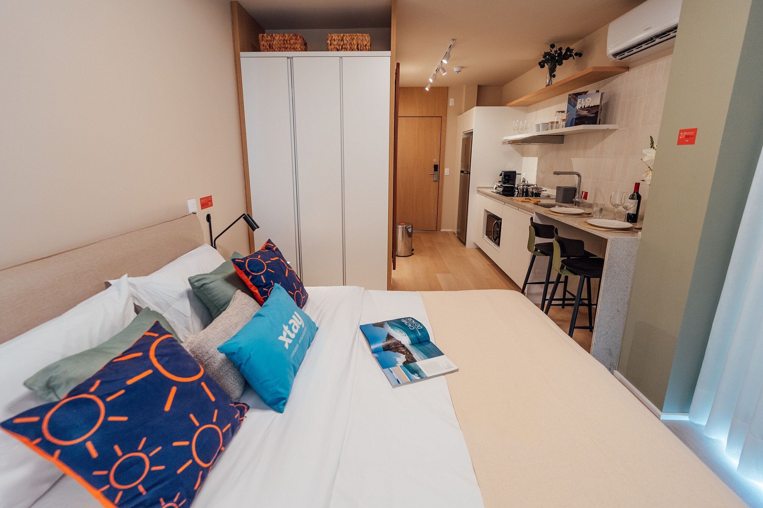A compact hotel room with a bed, a small kitchenette, and a separate bathroom.
