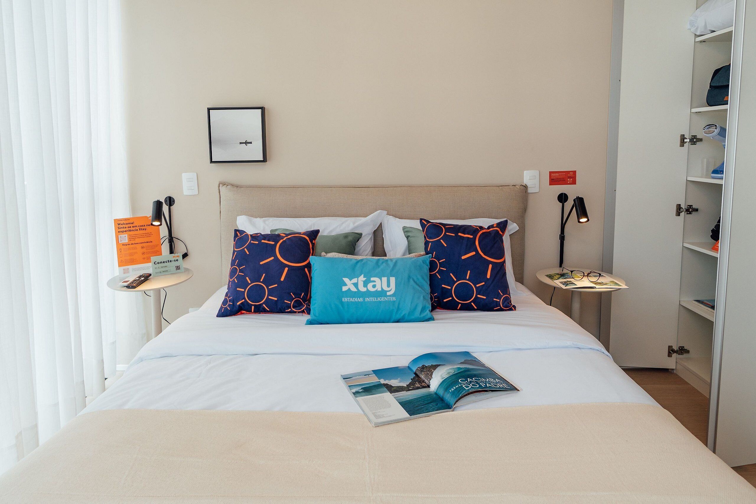 A hotel room with a bed, a nightstand, a reading lamp, and a shelf with personal items.