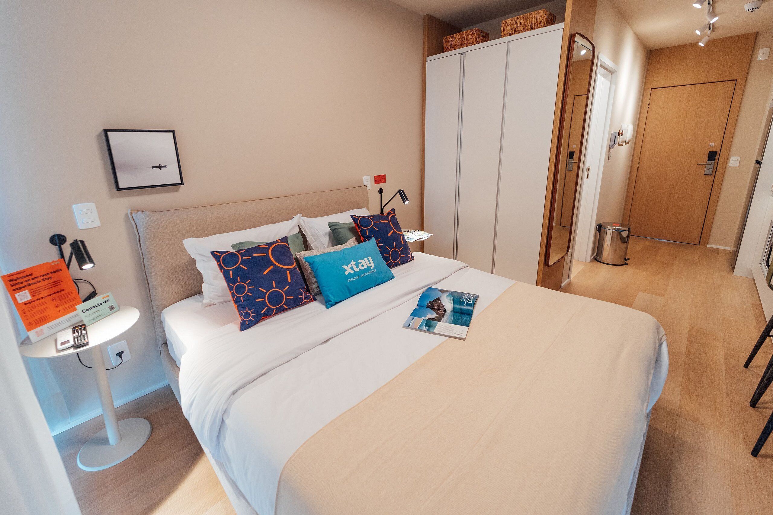 A neatly arranged hotel room with a bed, bedside table, and a wardrobe.