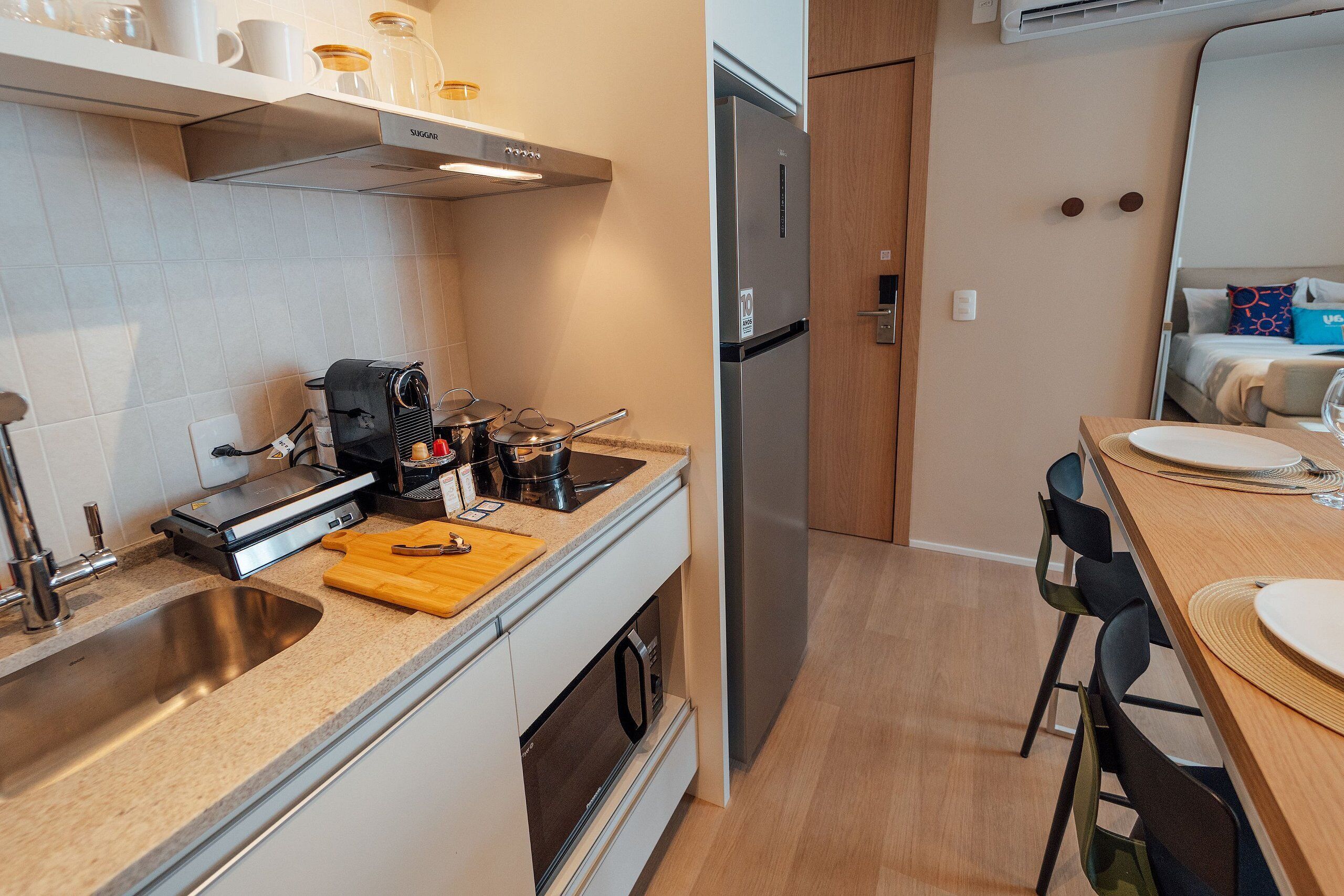A compact kitchen with a stainless steel sink, a coffee machine, a toaster, and a wooden cutting board.