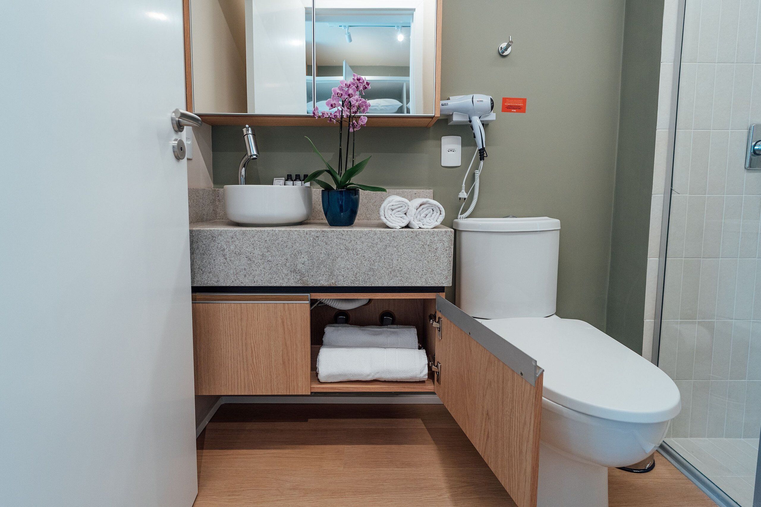 A modern bathroom with a white sink, a blue vase with flowers, a towel rack, and a toilet.