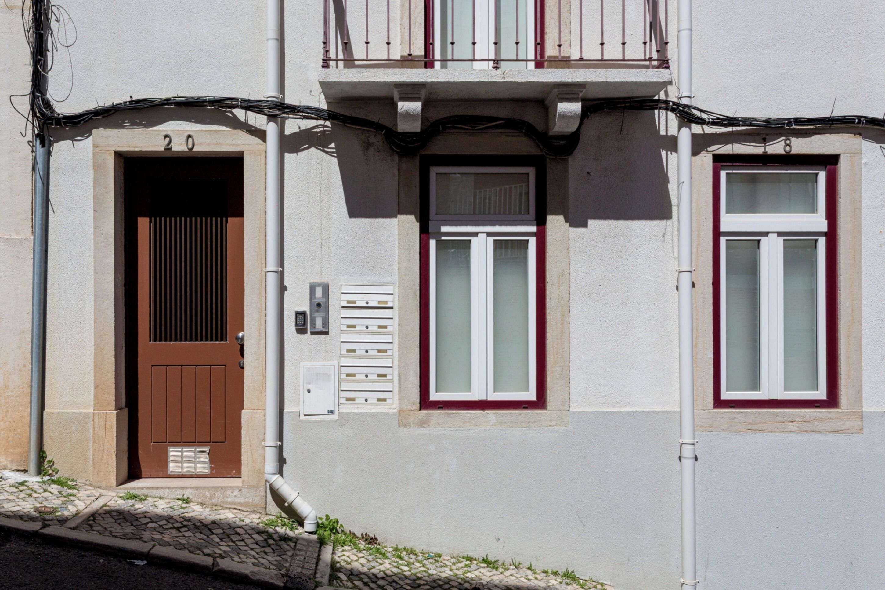 A building with a brown door, a window with white shutters, and a balcony with a railing.