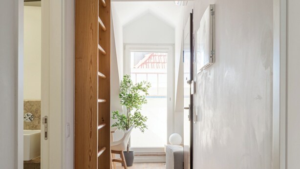 A hallway with wooden flooring, a plant, and a view of a room with a window. - Bridgeview Alcântara – The 3BR Loft Edition (Lisbon)