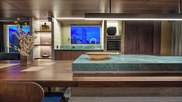A modern kitchen with a large island, built-in oven, and a view of a cityscape at dusk.