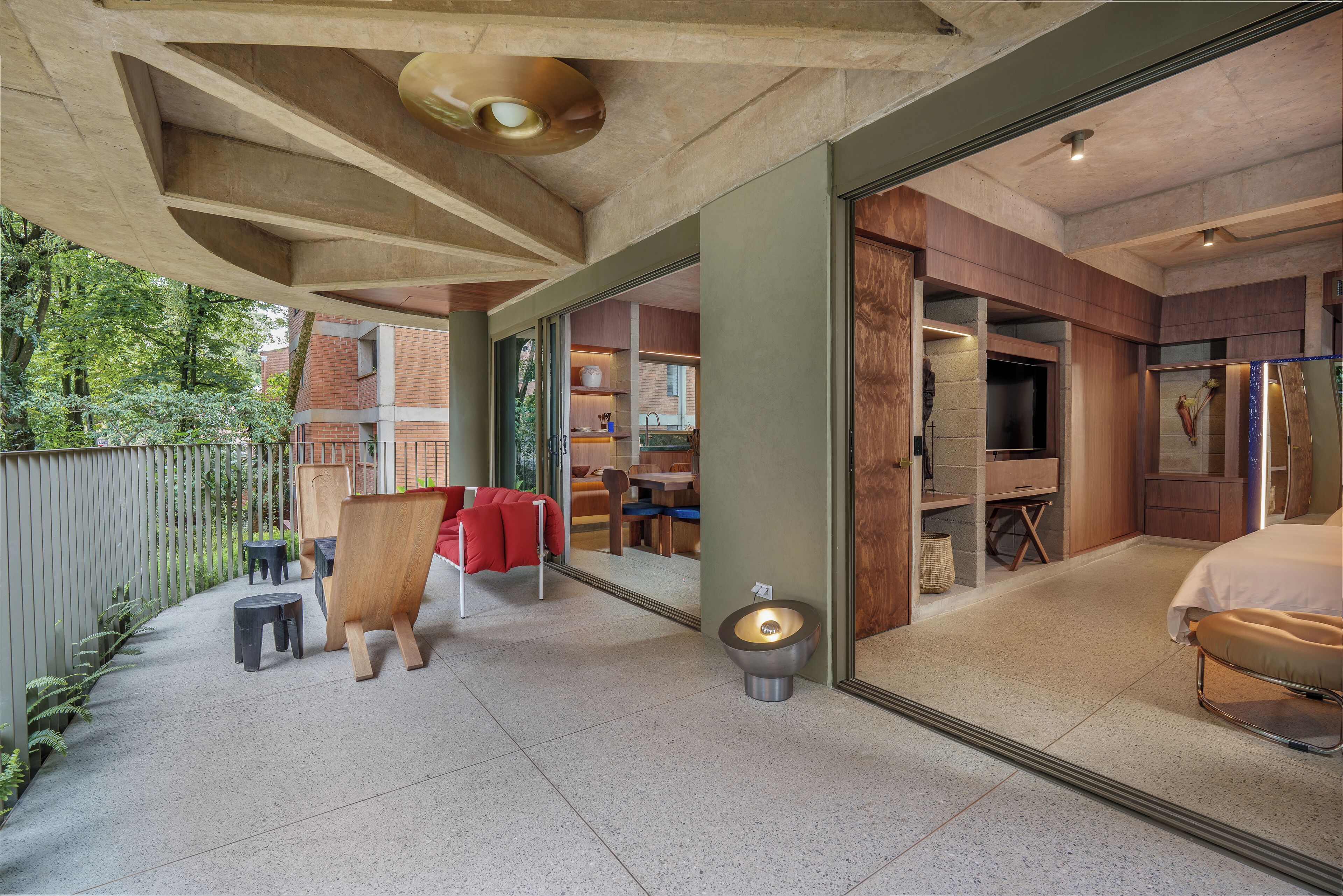 Un intérieur moderne agrémenté d’un grand miroir qui reflète une chambre, un coin cuisine et un espace détente avec des chaises rouges.