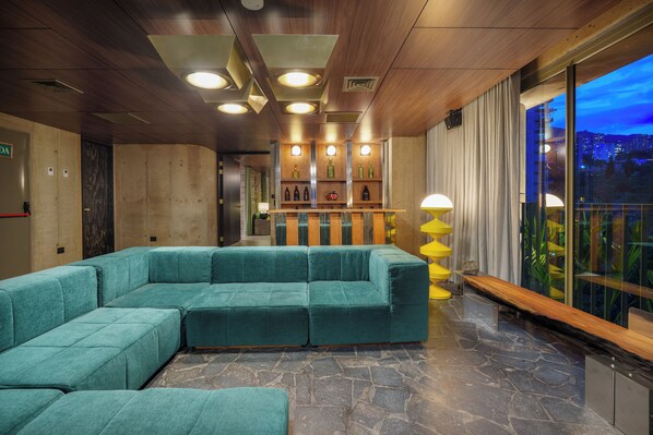 Una hall moderna con un divano componibile color petrolio, una scrivania in legno e un'ampia finestra con vista sulla città.