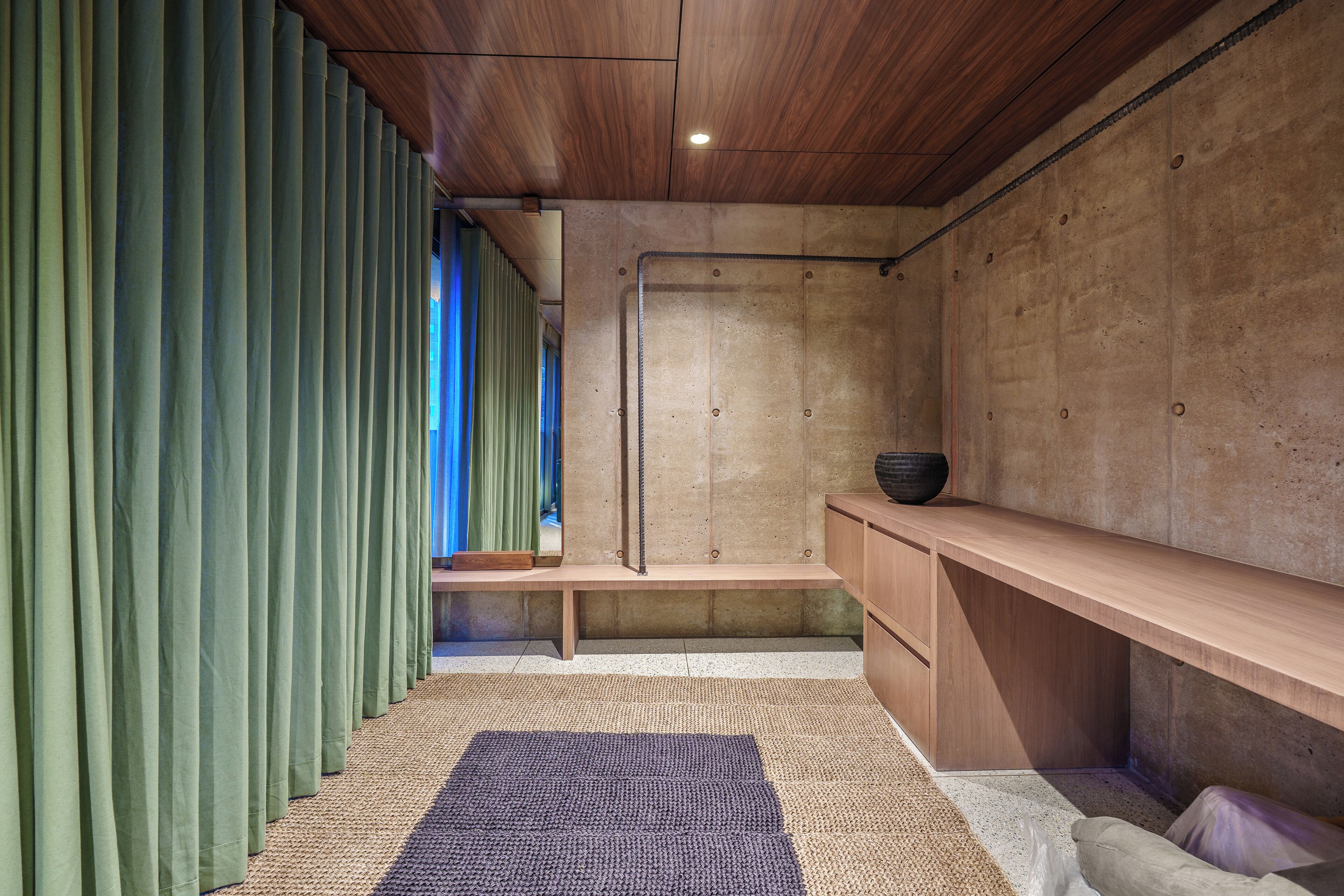 A modern bathroom with a wooden ceiling, a concrete wall, a bench, and a sink area.