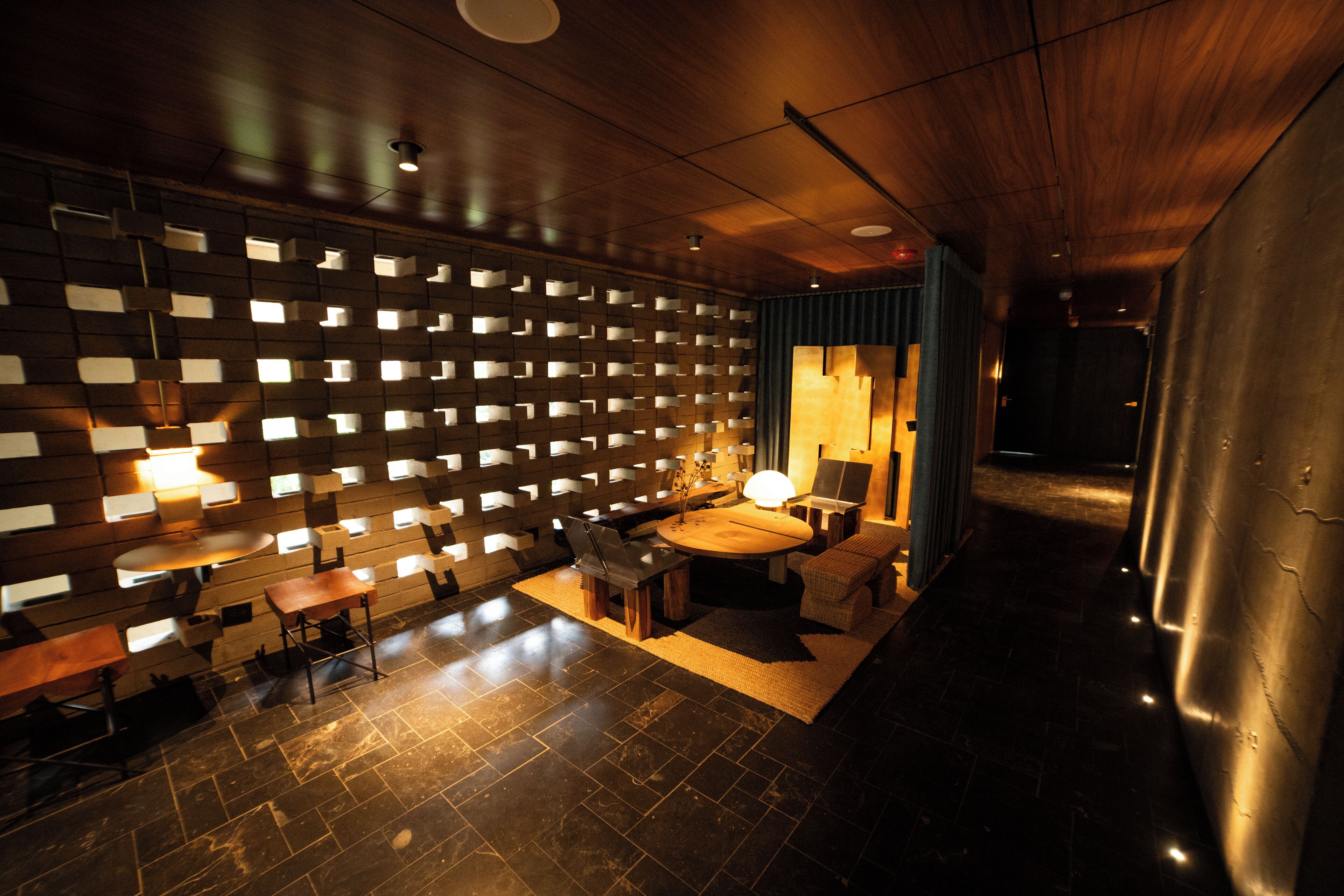 Un intérieur moderne avec un plafond en bois, un mur composé de panneaux lumineux, une table ronde entourée de chaises et un canapé.