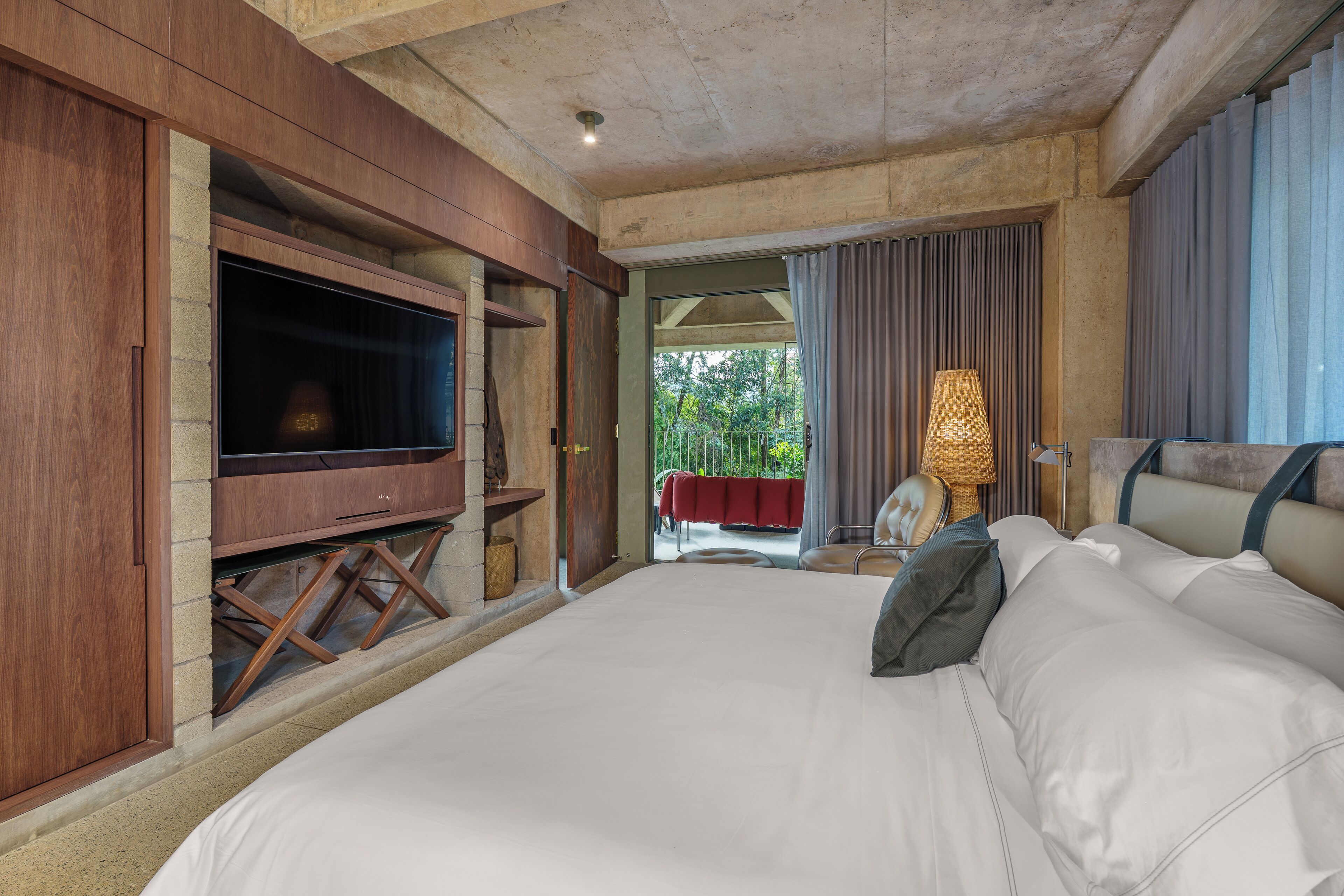 A large bed with white linens, a television on a wooden stand, and a view of the outdoors through a door.