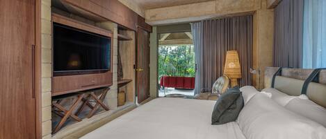 A large bed with white linens, a television on a wooden stand, and a view of the outdoors through a door.