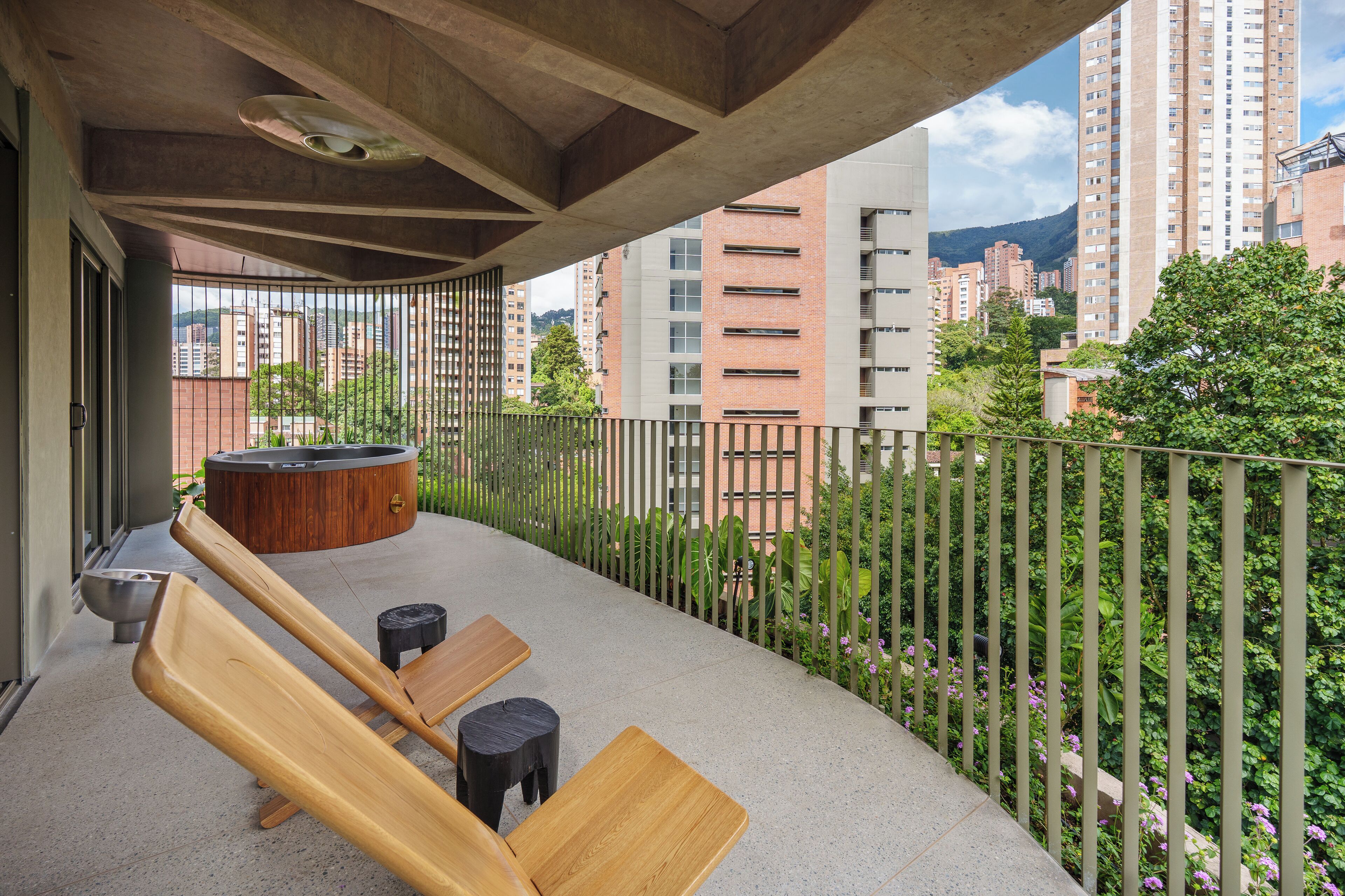 Un balcón con muebles de madera, una bañera de hidromasaje y vistas de edificios circundantes.